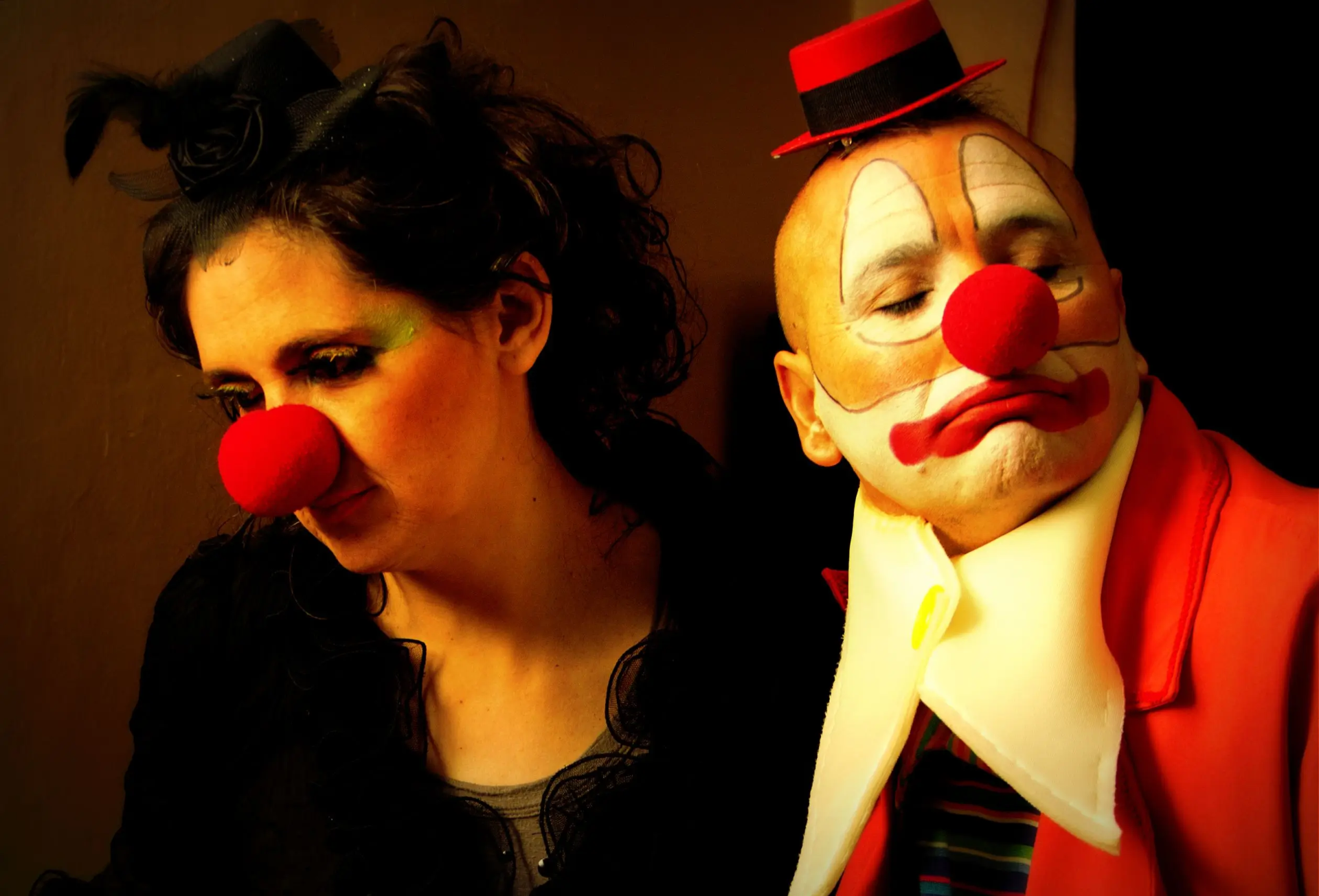 Dos personas vestidas y maquilladas de payaso, con las caras pintadas pero expresión seria y triste. 
